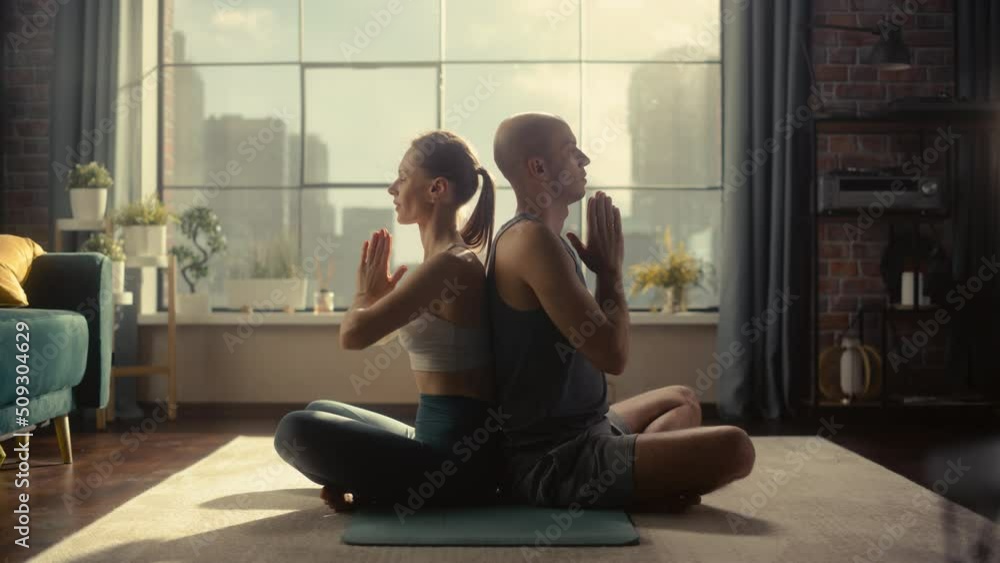 Young Athletic Couple Exercising, Practising Meditation in the Morning in Her Bright Sunny Home Living Room. Healthy Lifestyle, Fitness, Wellbeing and Mindfulness Concept. Young Athletic Couple Exercising, Practising Meditation in the Morning in Her Bright Sunny Home Living Room. Healthy Lifestyle, Fitness, Wellbeing and Mindfulness Concept.