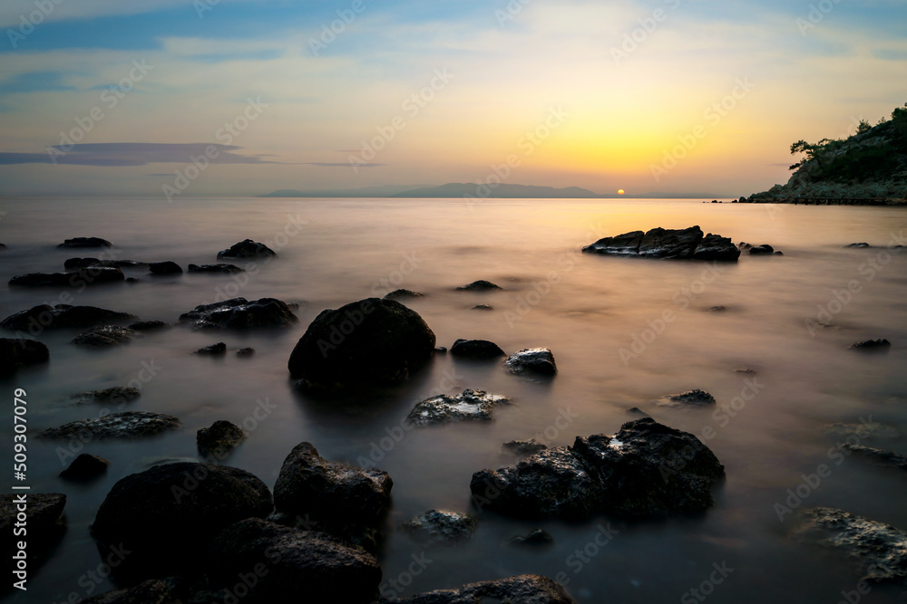 Long exposure photo of sea, rocks and sunset. Concept of relax, calm, tranquil and inner peace.