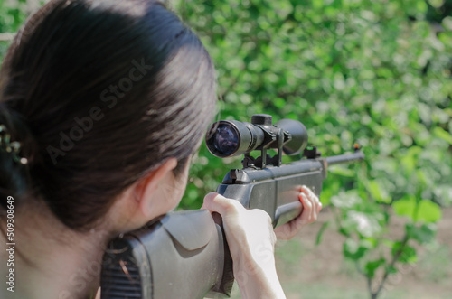 A sniper girl holds a gun in her hands. The hunter looks into the optical sight from behind. Looking through the scope of a sniper rifle