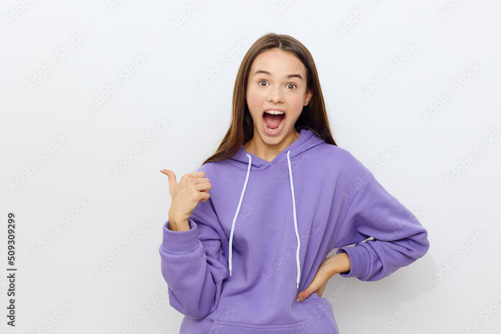 a happy woman stands on a white background in a purple tracksuit points her thumb behind her back with her mouth wide open and her other hand on her hip a happy woman stands on a white background in a purple tracksuit points her thumb behind her back with her mouth wide open and her other hand on her hip