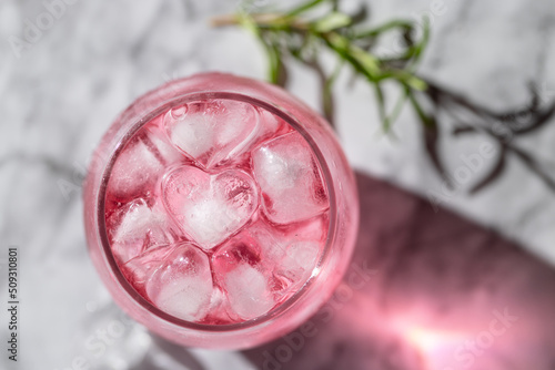 The glass of pink drink with ice and rosemary on background