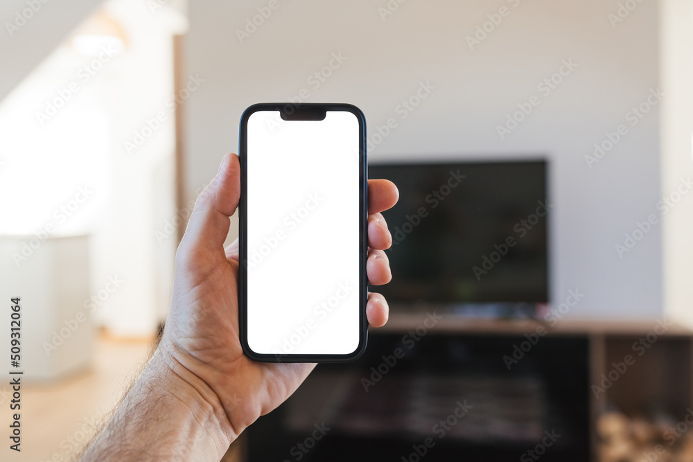 Man holding smartphone with blank white mockup screen in front of flat screen television set