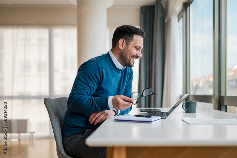 Smiling businessman working on laptop while sitting at office desk Smiling businessman working on laptop while sitting at office desk