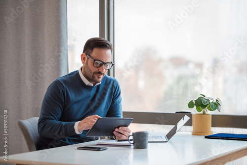 Businessman using digital tablet while working on laptop at desk