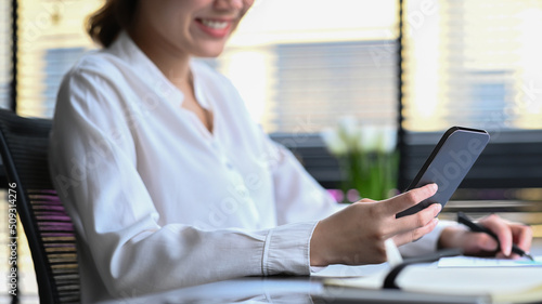 Smiling working woman sitting at her office desk and using smart phone