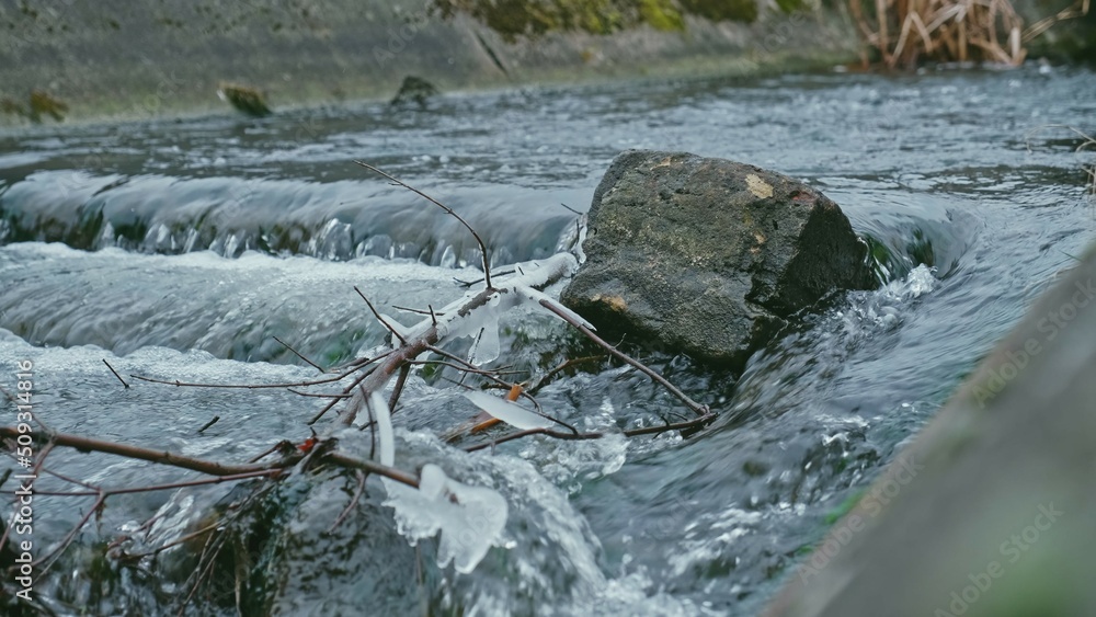 Fototapeta premium Crystals of Ice and Icicles Forming on Bank of Fast Flowing Clean Water Stream on Cold Day 