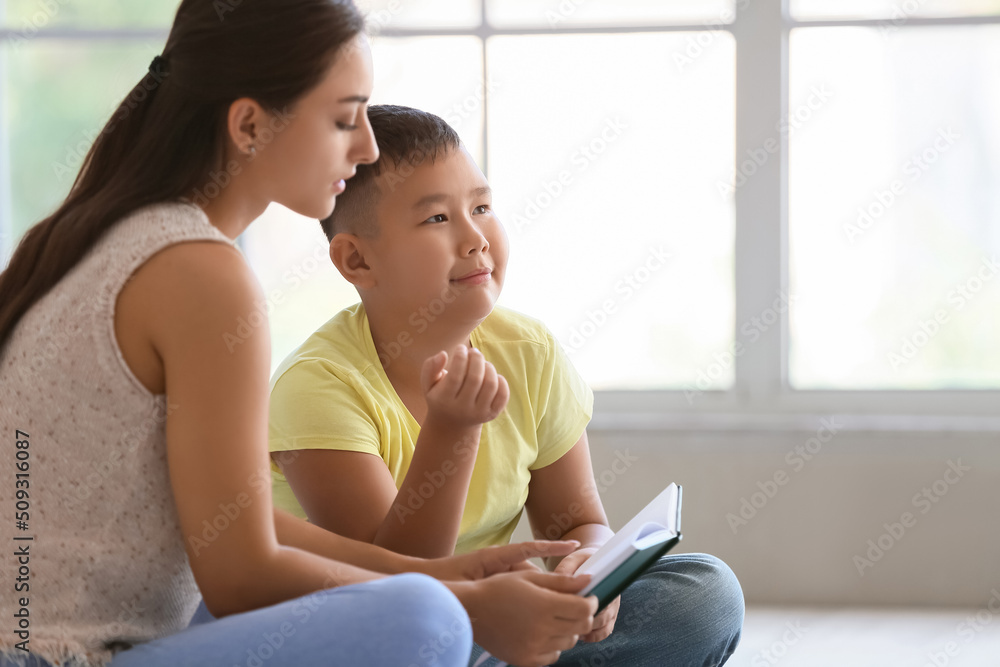 Little Asian boy reading book with his teacher in classroom Little Asian boy reading book with his teacher in classroom