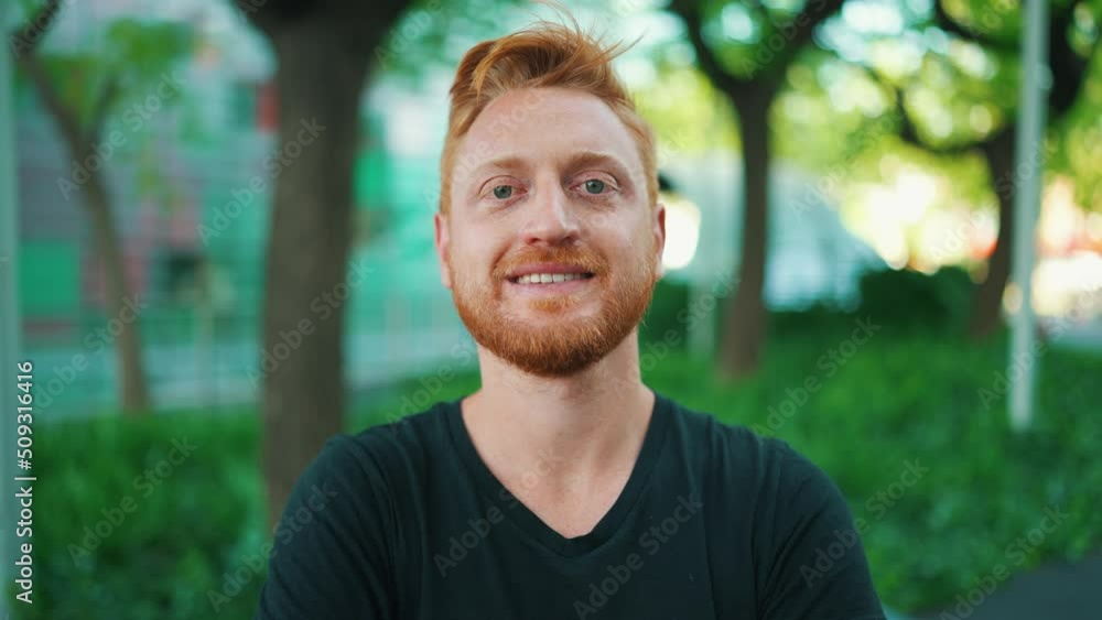 Smiling red haired man looking at the camera while standing in the park Smiling red haired man looking at the camera while standing in the park