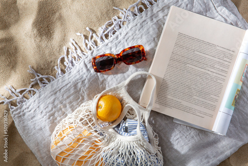 leisure and summer holidays concept - bag of oranges, sunglasses and magazine on blanket on beach sand