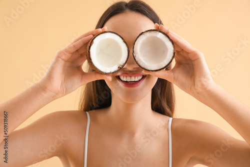 Funny young woman with coconut on beige background