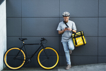 Express food delivery courier with insulated bag looking at phone.