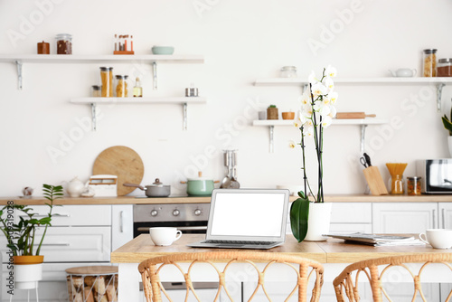 Modern laptop and orchid flower on dining table in kitchen