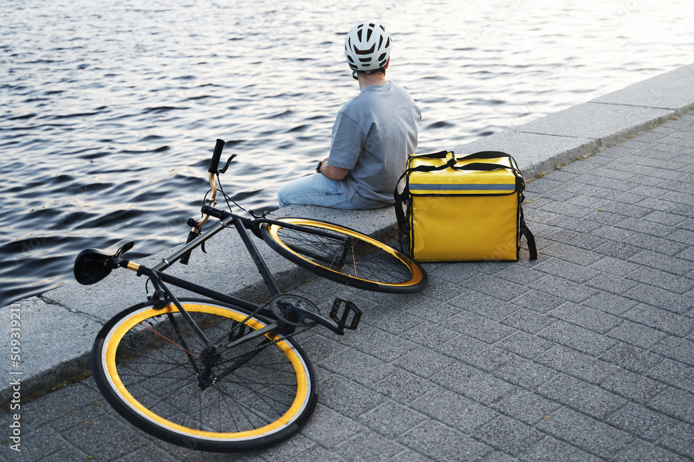 Fototapeta premium Express delivery courier sitting on quay looking at river.