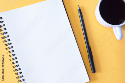 Directly above view of notepad, pen and coffee cup on yellow background.