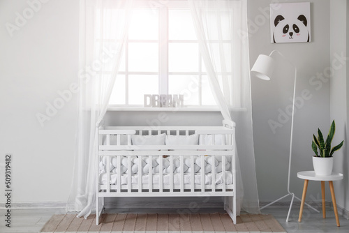 Interior of light nursery with baby crib, lamp and window