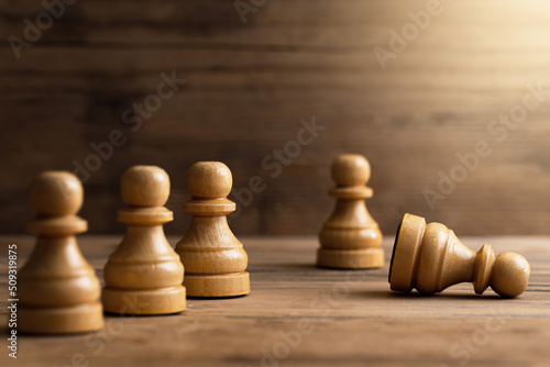 Fotografiet Wooden chessmen standing with one chess pawn lying.