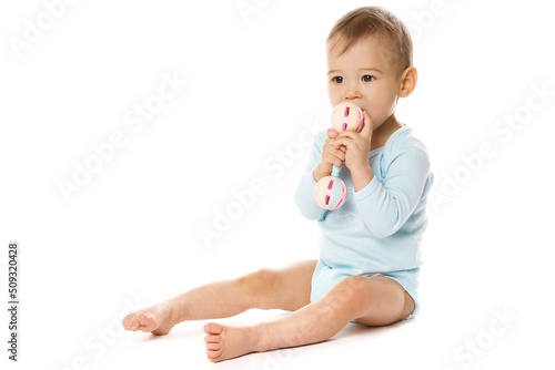Little boy in romper sitting and playing with plastic rattle. © blackday