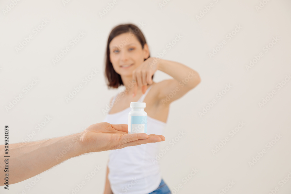 Young smiling woman advertising remedy for male potency close up, white blurred background. Holding in hand and pointing at jar of pills, impotence treatment. Male health and sexual attraction Young smiling woman advertising remedy for male potency close up, white blurred background. Holding in hand and pointing at jar of pills, impotence treatment. Male health and sexual attraction