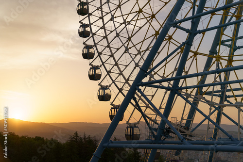 Famous ferris wheel in Mtatsminda amusement park in Tbilisi, Georgia. Giant wheel with cabins at sunset, mountain on background. Entertainment concept