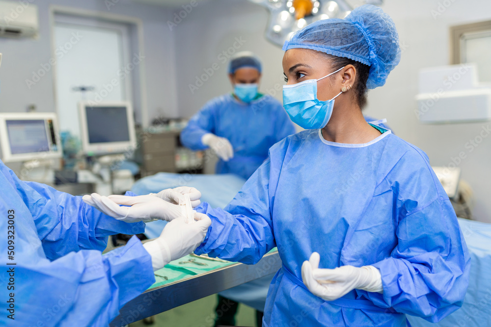 Young nurse in protective mask and workwear helping surgeon with gloves while both preparing for operation Young nurse in protective mask and workwear helping surgeon with gloves while both preparing for operation