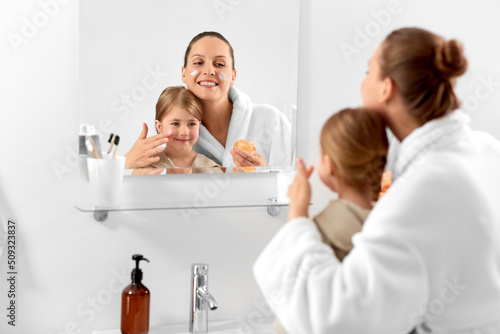 beauty, family and people concept - happy smiling mother and daughter with moisturizer in bathroom
