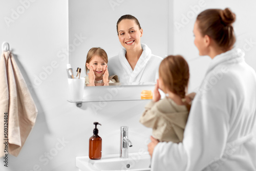 beauty, hygiene and people concept - happy smiling mother and daughter with moisturizer in bathroom
