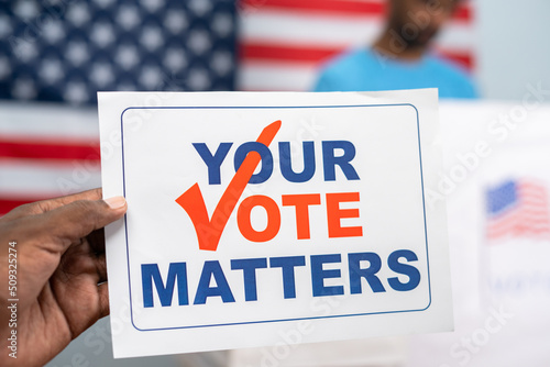 close up shot of hands holding your vote matter in front of polling or voting station - concept of responsibility and campaign.