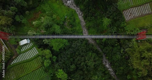 aerial drone view of fly over metal suspension bridge that builds crossing the valley and river with terraced waterfall. road connection video. 4K infrastructure photo