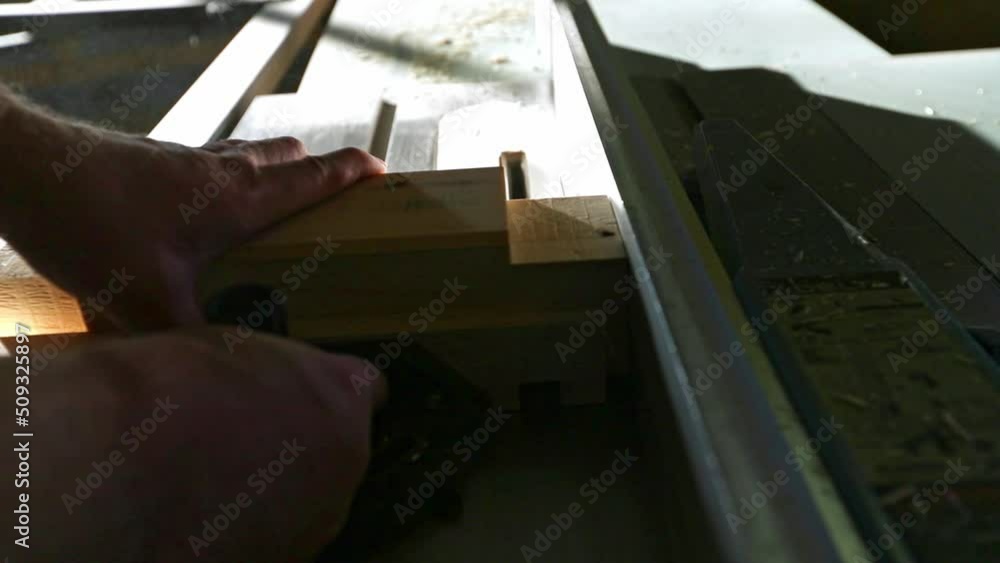 A woodworker places a piece of wood on a table saw with a stacked dado set and pushes it through to make multiple cuts to create a tenon in slow motion. A woodworker places a piece of wood on a table saw with a stacked dado set and pushes it through to make multiple cuts to create a tenon in slow motion.