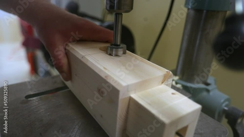 Drilling out a tenon slot in a wood beam on a drill press in slow motion as wood chips are displaced in every direction. photo