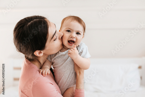 Closeup portrait of loving young mom kissing little kid in cheek  bonding with her adorable son or daughter  free space