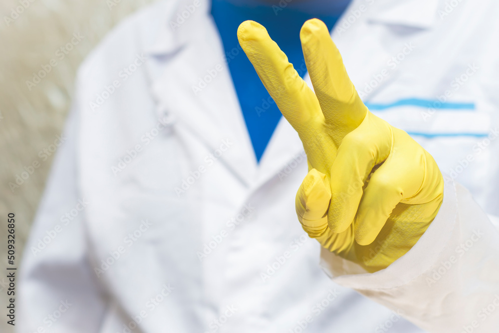 A doctor in a medical gown and protective gloves shows a sign of victory. The face is not visible. A doctor in a medical gown and protective gloves shows a sign of victory. The face is not visible.