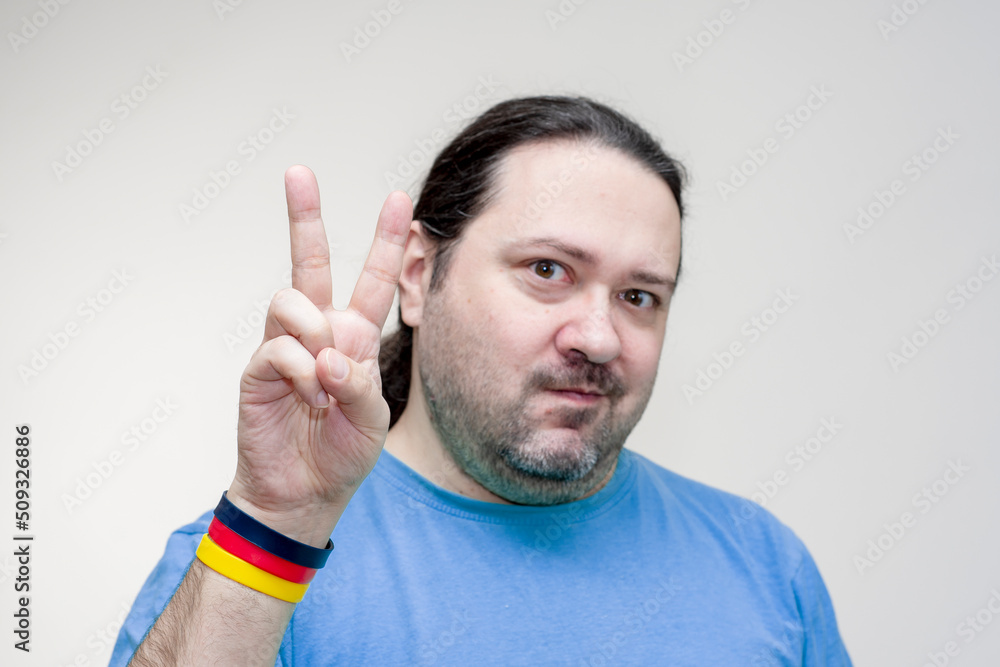 An adult, unshaven man in a T-shirt shows a sign of victory with his fingers. Bracelet in the colors of the German flag. An adult, unshaven man in a T-shirt shows a sign of victory with his fingers. Bracelet in the colors of the German flag.