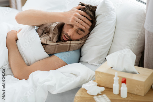 people and health problem concept - unhappy sick man having headache lying in bed at home