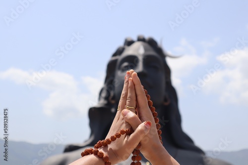 A lady hands surrounded by Rudraksha, praying scene in front of the blurred statue of Adiyogi Shiva. photo