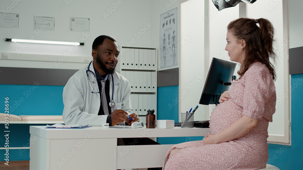 General practitioner consulting woman expecting child in office, attending examination appointment. Male physician having private conversation about pregnancy with pregnant patient.