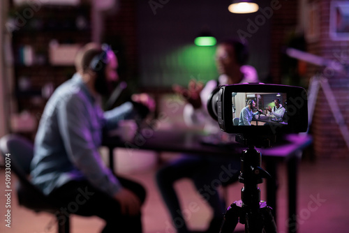Multiethnic team of people meeting to broadcast internet podcast, recording video discussion on camera. Influencer and guest talking on online livestream to create social media channel content. photo