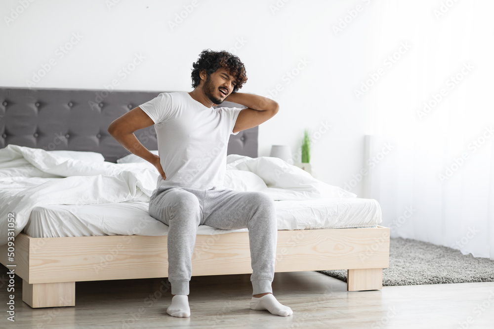 Unhappy man suffering from back pain, sitting on bed Unhappy man suffering from back pain, sitting on bed
