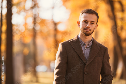 a man in classic clothes poses outdoors against the background of yellow autumn tree leaves