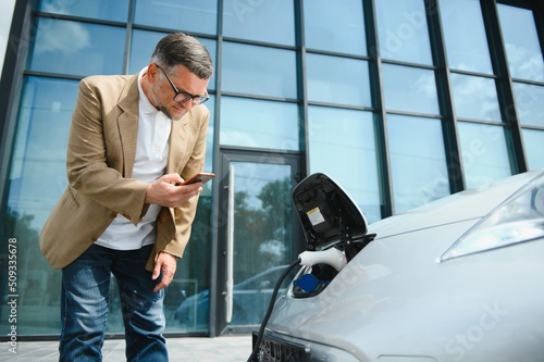 Handsome man using phone while car being charged