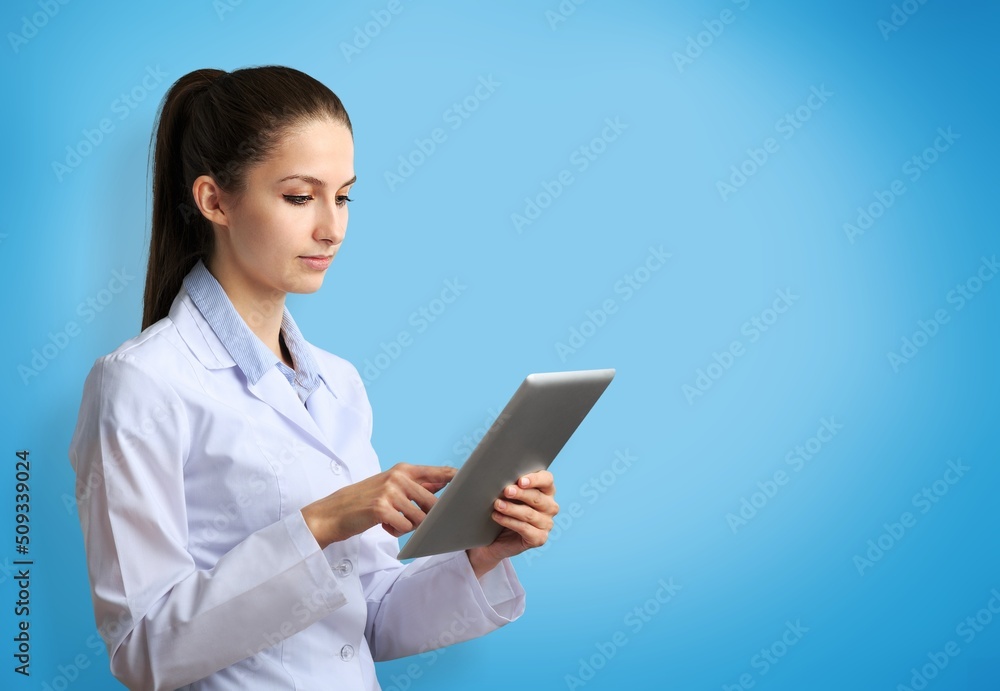 Beautiful young girl doctor, with digital table on a blue background. Medical student practitioner. The concept of medical education Beautiful young girl doctor, with digital table on a blue background. Medical student practitioner. The concept of medical education