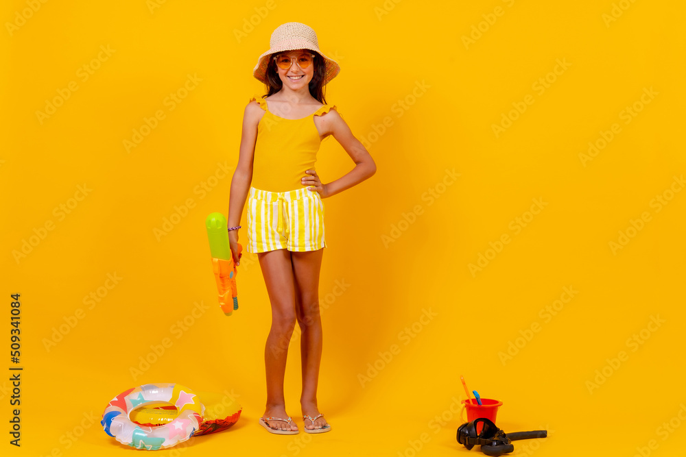 Little girl playing with summer toys on a yellow background