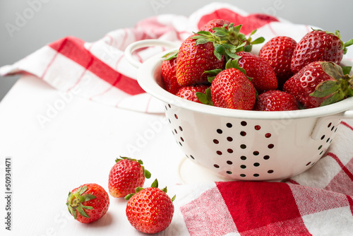 Tablou pe pânză Aerial view of strawberries in a white colander on a white table with a red kitc