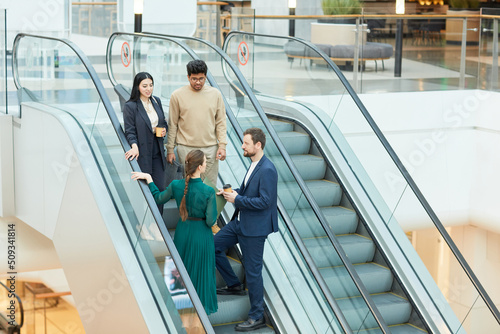 Wide angle view at group of business people standing on escalator in office building and communicating, copy space