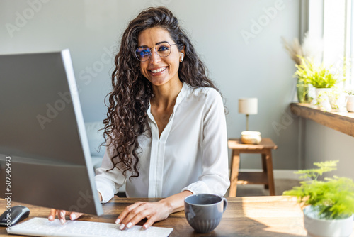 Successful businesswoman standing in creative office and looking at camera. Young latin woman entrepreneur in a coworking space smiling. Portrait of beautiful business woman  photo