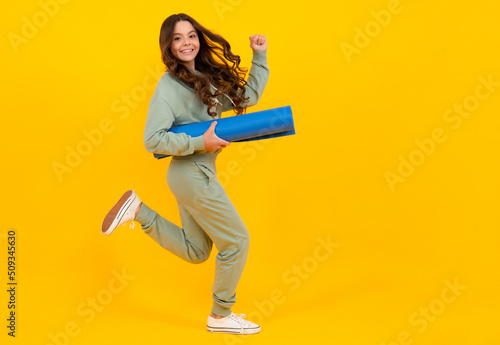 Child girl dressed in sports uniform. Child in a posh stylish sports suit in a hoodie with a hood hold yoga mat. Run and jump. Advertising sportswear tracksuit. Healthy kids lifestyle, sport.