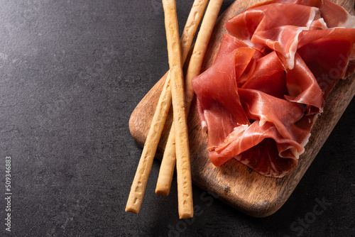 Spanish serrano ham with olives and breadstick on black background. Copy space