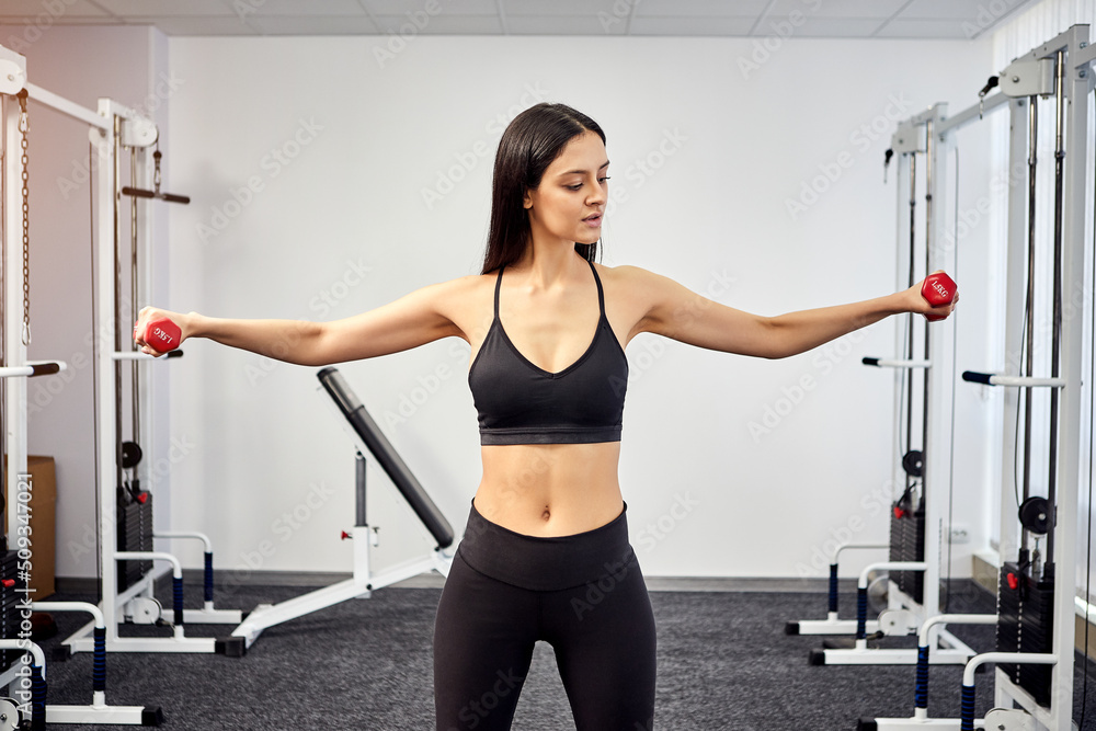 Fototapeta premium Beautiful Female patient trains in rehabilitation kinesio clinic using dumbbells