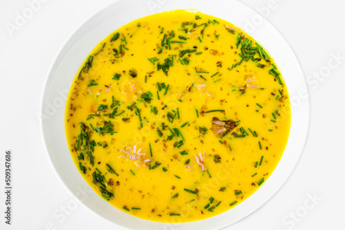 Creamy yellow vegetable soup in white plate on white.