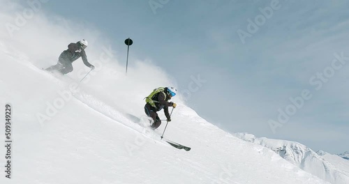 Two male ski athletes performing a great ski show in a beautiful ski resort in the tyrolean mountains. Alpine downhill skiing in great rythm and perfect ski style. Fresh snow follow camera skiing 4K. photo